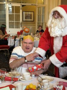 Father Christmas hands a gift to Sam at the Continued Care Christmas Luncheon 2025 in Harrogate